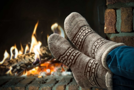 Feet in warm, patterned socks, resting by a fireplace with a fire.