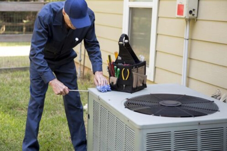 A man in work clothes is cleaning an air conditioner outdoors.